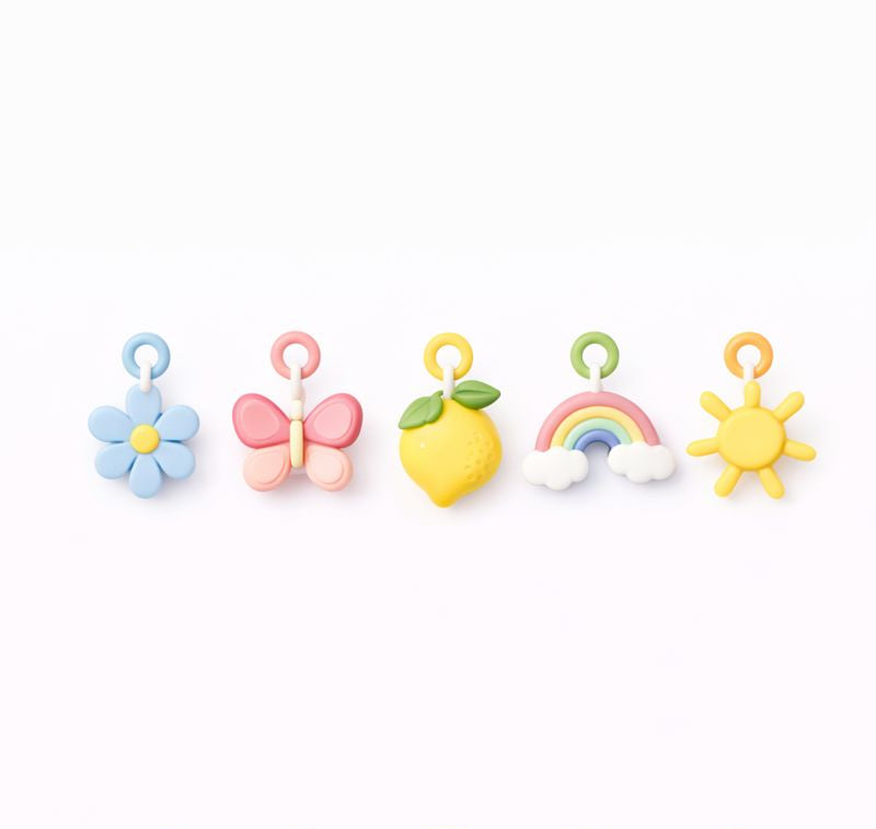 Set of colorful children's charms including a flower, butterfly, lemon, rainbow, and sun on a white background.
